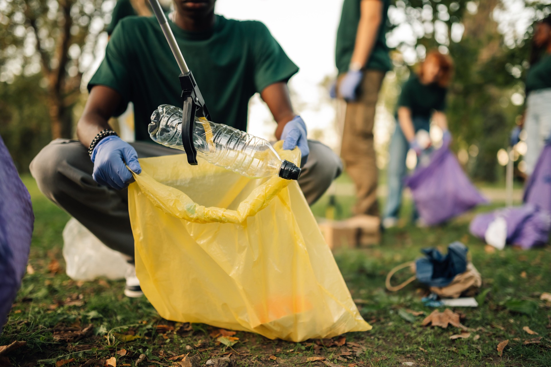 Volunteer picking up plastic bottle in park cleanup